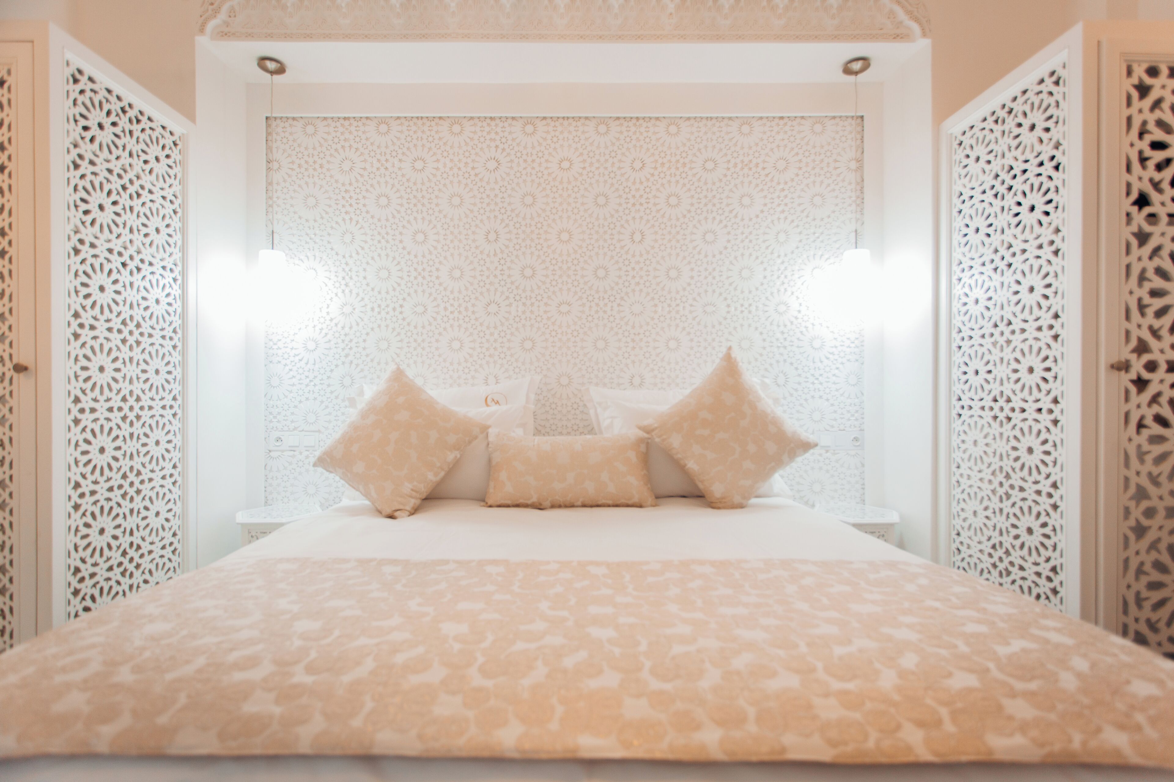 Una cama con colcha estampada y tres almohadas, un techo decorativo y una pared adornada.
