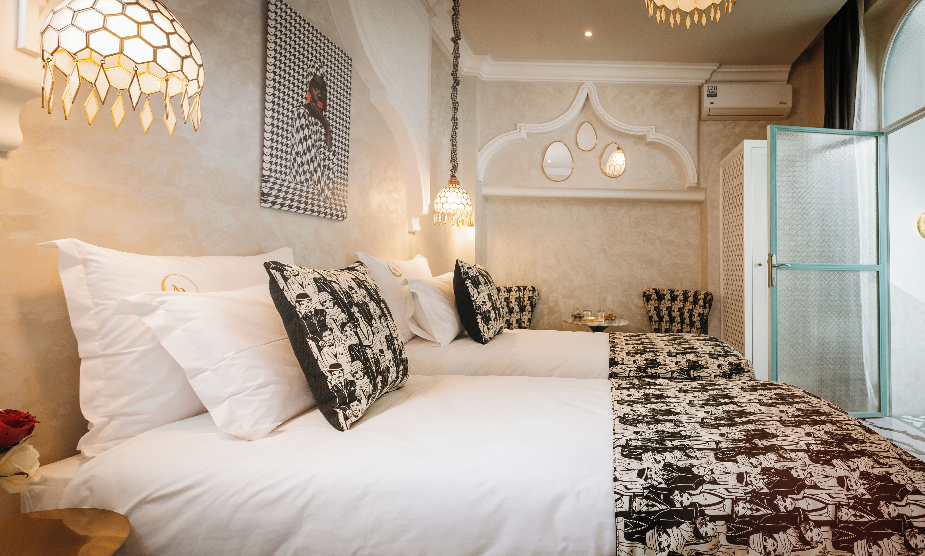 A hotel room with a large bed, a bedside table, a chair, a wall-mounted lamp, and a door with a frosted glass panel.