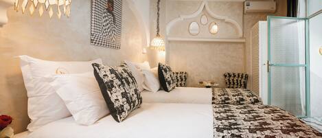 A hotel room with a large bed, a bedside table, a chair, a wall-mounted lamp, and a door with a frosted glass panel.