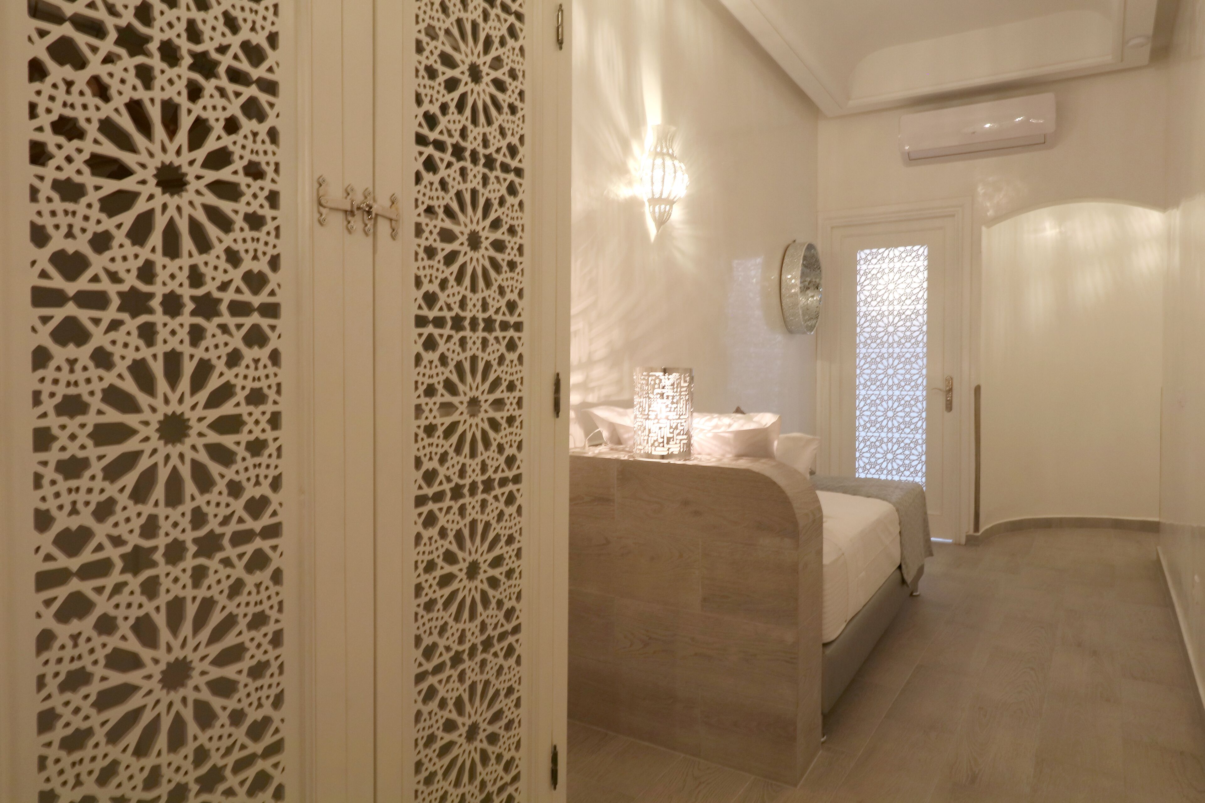 Une chambre à coucher comprenant un lit, une table de chevet, une lampe fixée au mur et une porte décorative.