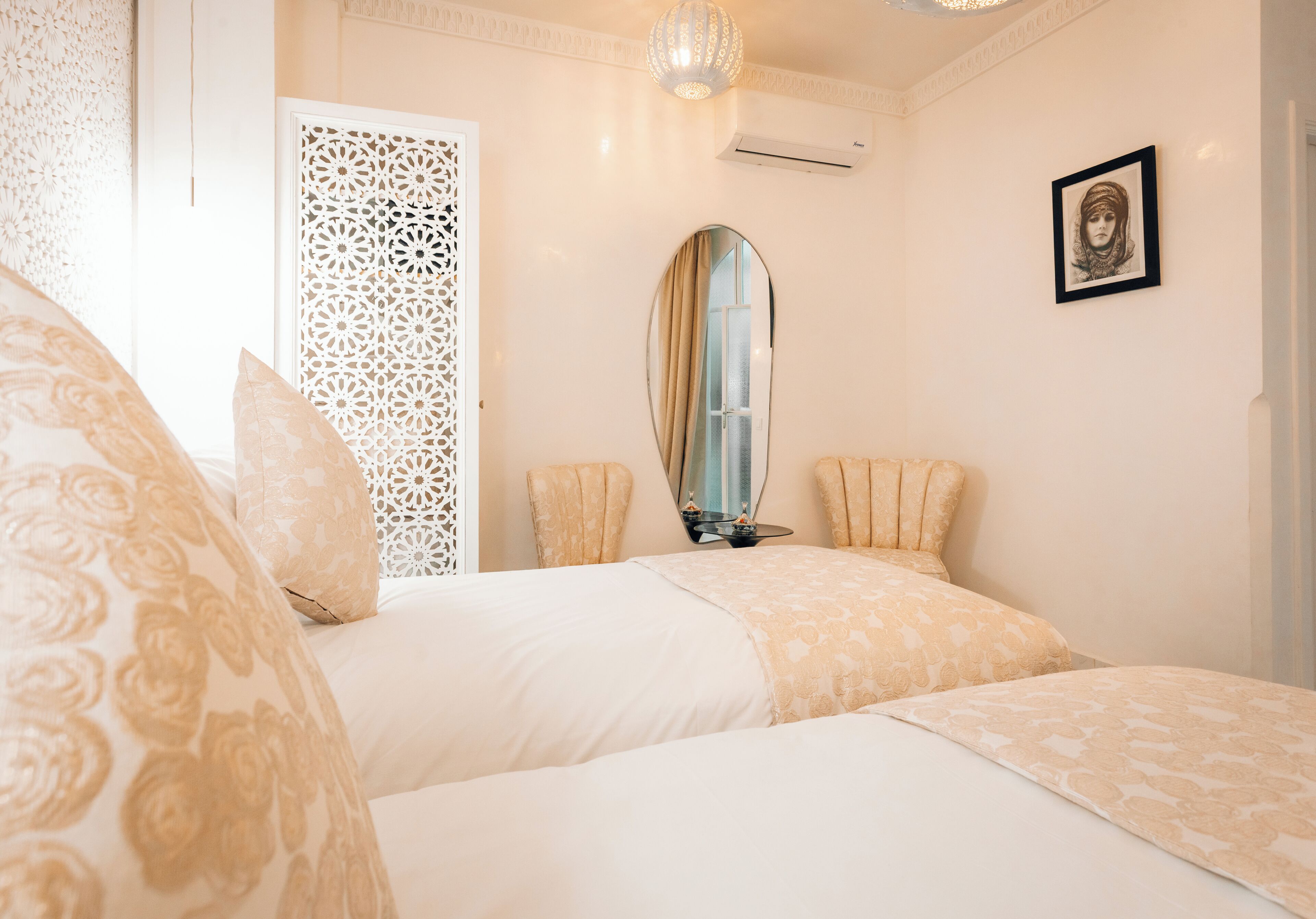 A hotel room with a bed, a mirror, a framed picture on the wall, and a decorative screen.