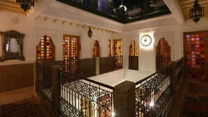 A traditional interior with a central courtyard, ornate wooden doors, and a balcony with a view of the night sky.
