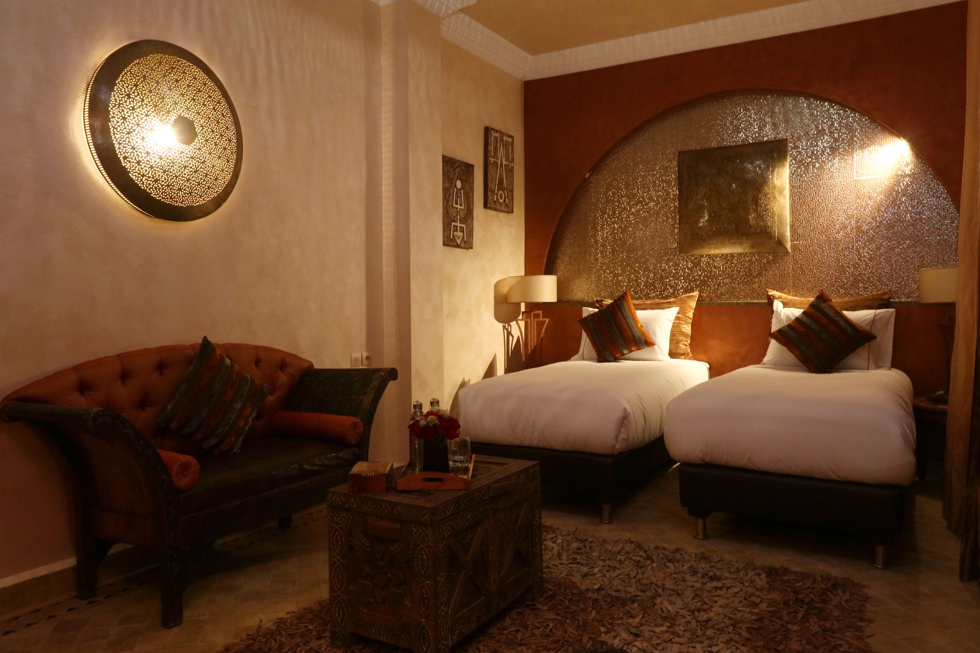 A hotel room with two beds, a sofa, a coffee table, and decorative wall lighting.