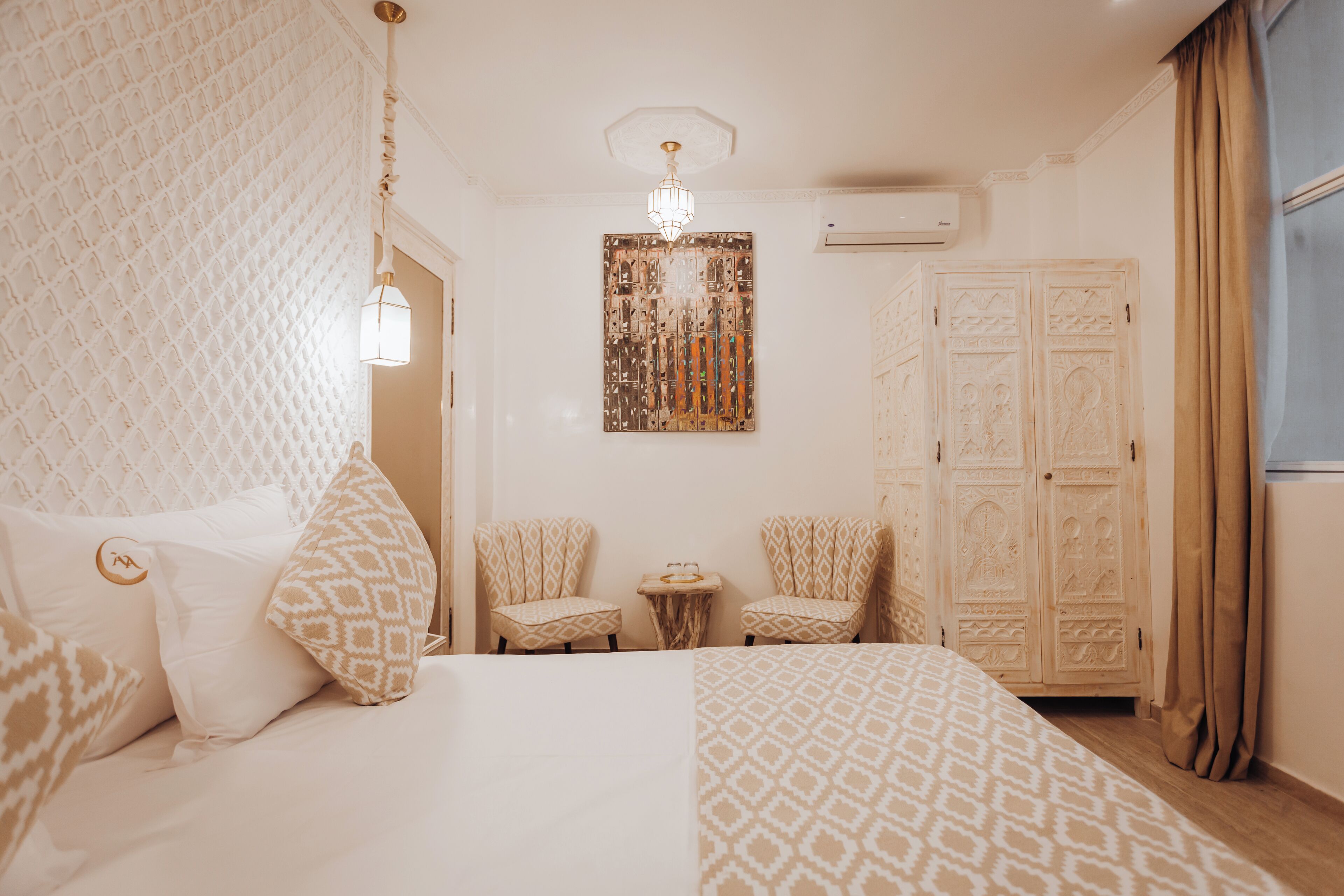 A hotel room with a large bed, two armchairs, a small table, and a decorative wall piece.