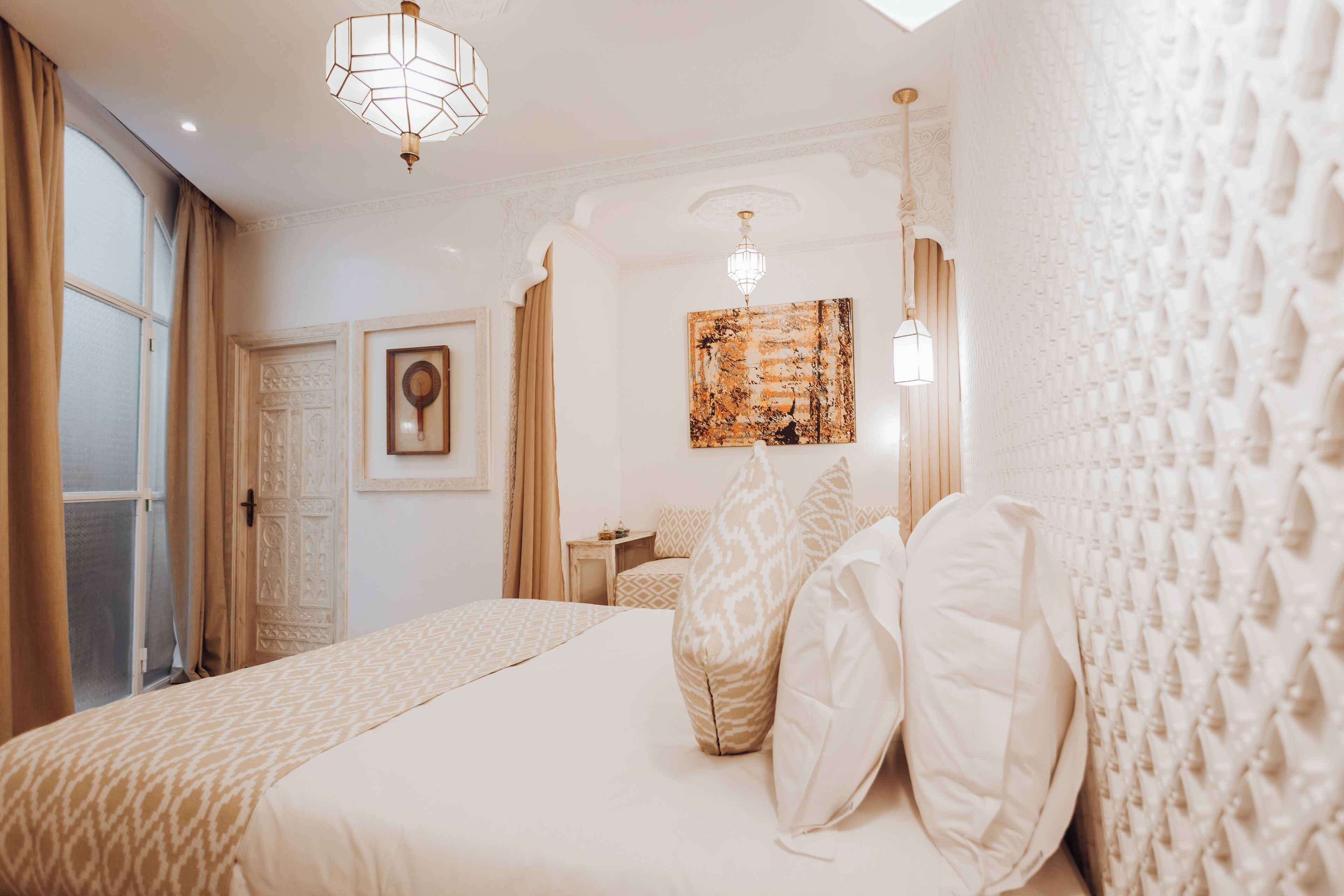 A bedroom with a large bed, a chandelier, a painting, and a patterned wall.
