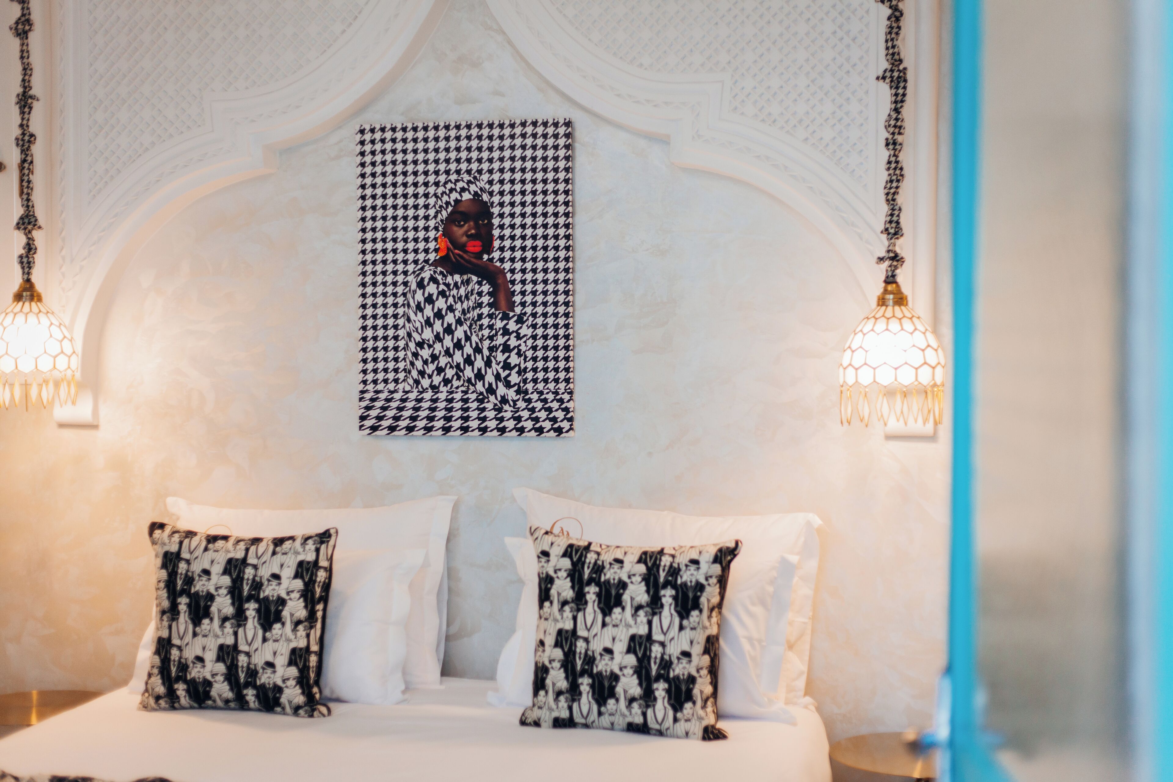 Quarto de hotel com cama, duas almofadas estampadas, uma obra de arte na parede e duas arandelas.