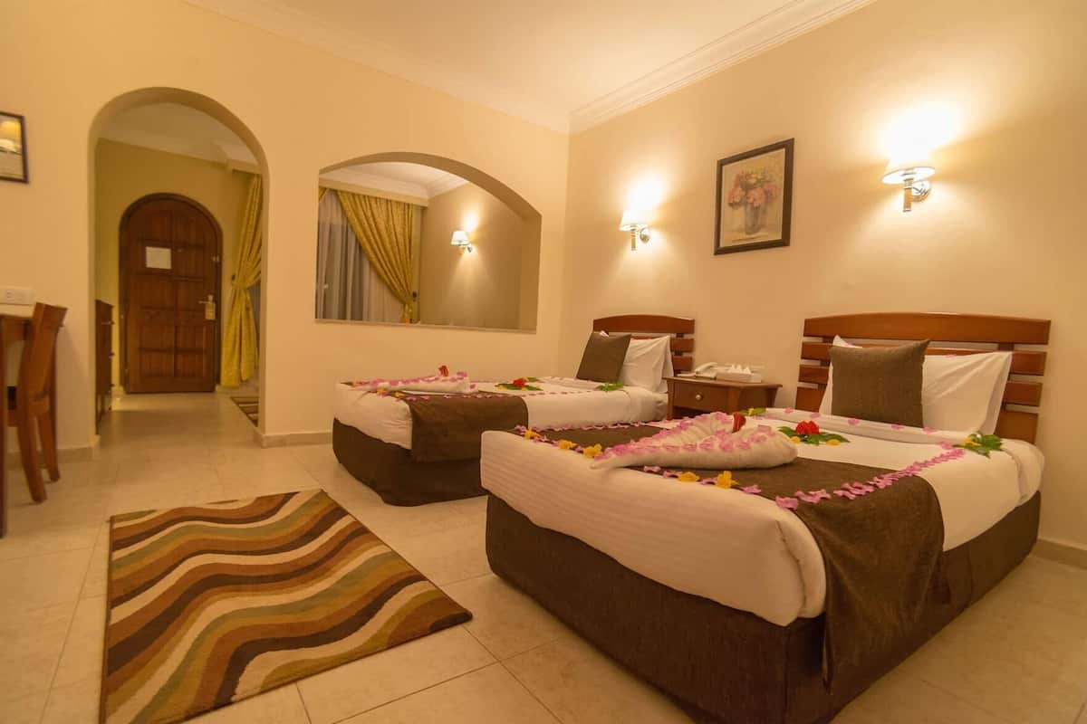 A hotel room with two beds, a desk, a chair, a striped rug, and a mirror.