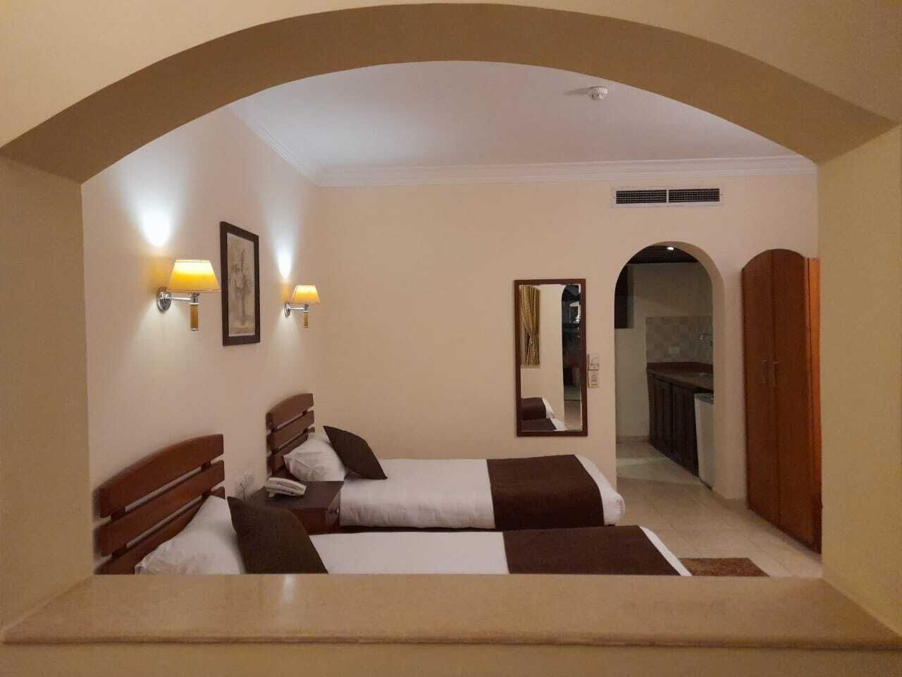 Habitación de hotel con dos camas, un área de descanso, un espejo y vista a la cocina.