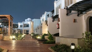 A pathway leading to a building with white walls and satellite dishes, surrounded by greenery and outdoor lighting.