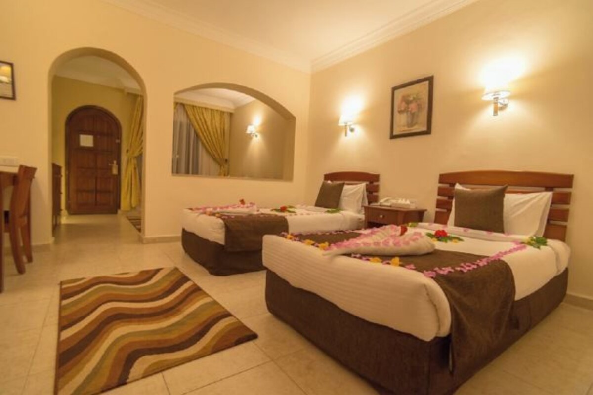 Quarto de hotel com duas camas, área de estar e banheiro.