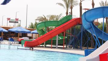 A pool area with multiple slides, a restaurant/bar sign, and palm trees in the background.