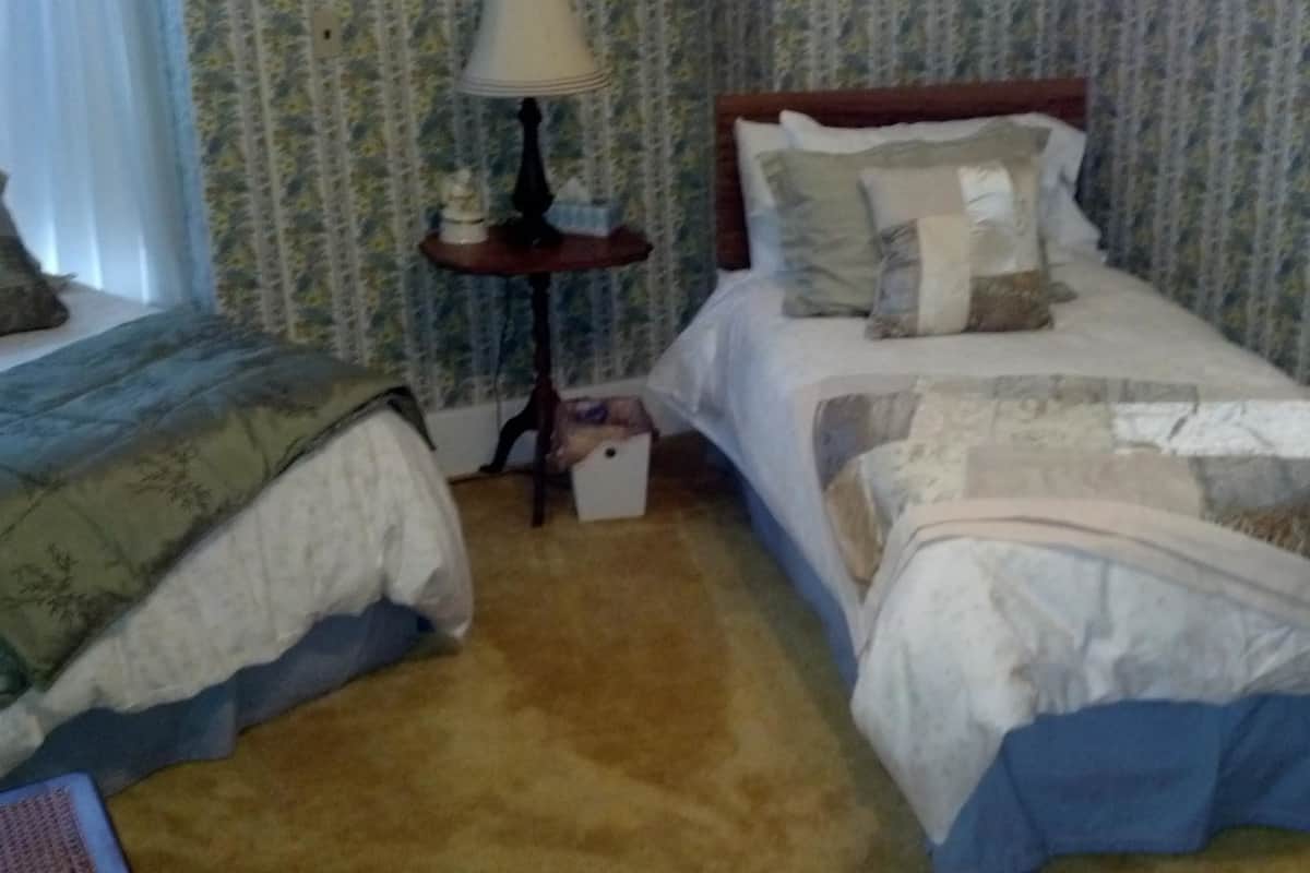 A hotel room with two single beds, a nightstand with a lamp, and a small table with a box.