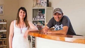 A woman in a white dress standing next to a counter with a man leaning on it. There are shelves with various items in the background. - Cabañas y Spa Costa Patagonia (Pichilemu)