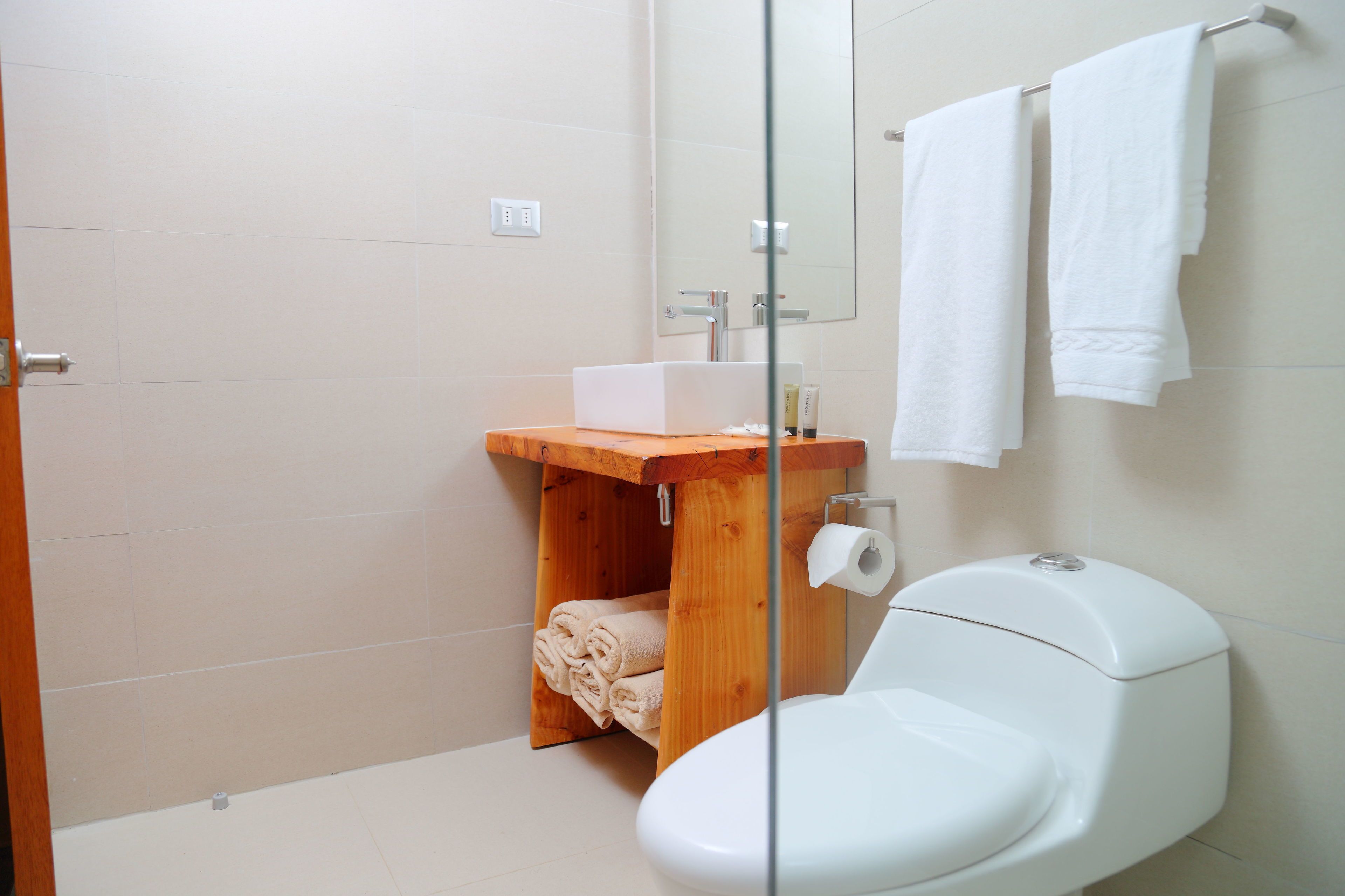 A bathroom with a wooden vanity, a toilet, and a glass shower enclosure.