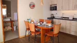 A compact kitchen with wooden cabinets, a microwave, and a sink. Adjacent is a dining area with wicker chairs and a round table set for four. - Cabañas y Spa Costa Patagonia (Pichilemu)
