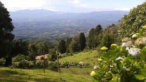 A lush green landscape with a view of distant mountains and a small building in the foreground. - Lagunillas del Poas (San Juan)