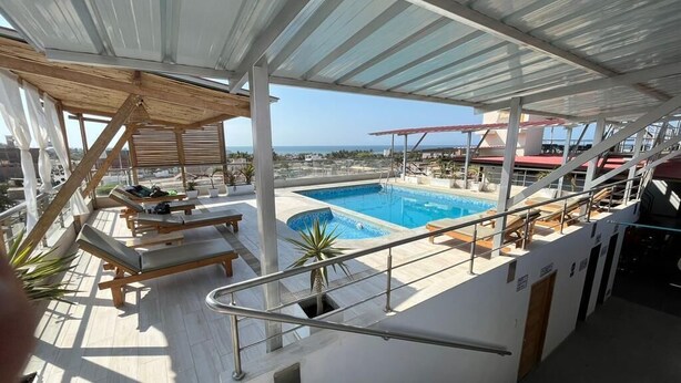Un área de piscina en la azotea con sillones de descanso y una escalera que lleva a una terraza superior.