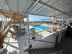 Un área de piscina en la azotea con sillones de descanso y una escalera que lleva a una terraza superior.
