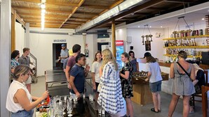 Evento social en un espacio interior moderno con vigas de madera en el techo, zona de bar con botellas, y señalización visible de servicios sanitarios.