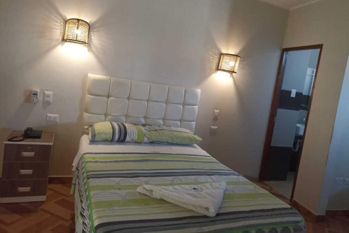 A bedroom with a large bed, two wall-mounted lamps, a bedside table, and a mirror.