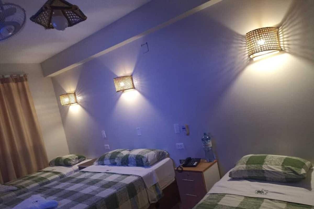 A room with two beds, each with a checkered bedspread, a nightstand with a lamp, and a wall-mounted light fixture.