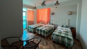 Habitación con dos camas, una mesa y sillas. Hay cortinas y un ventilador de techo.