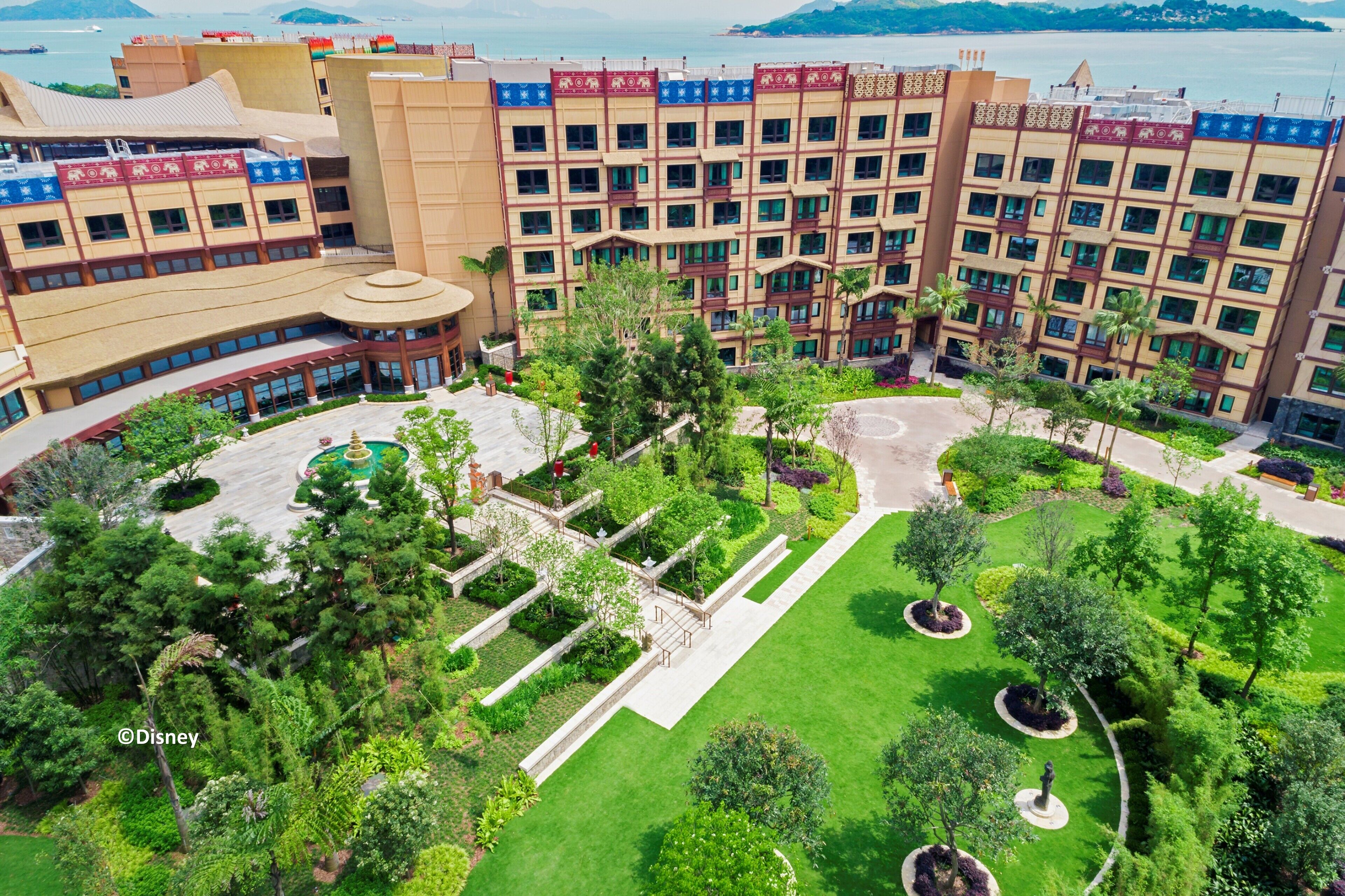 A hotel with multiple floors, a central courtyard with greenery, and a view of the sea.