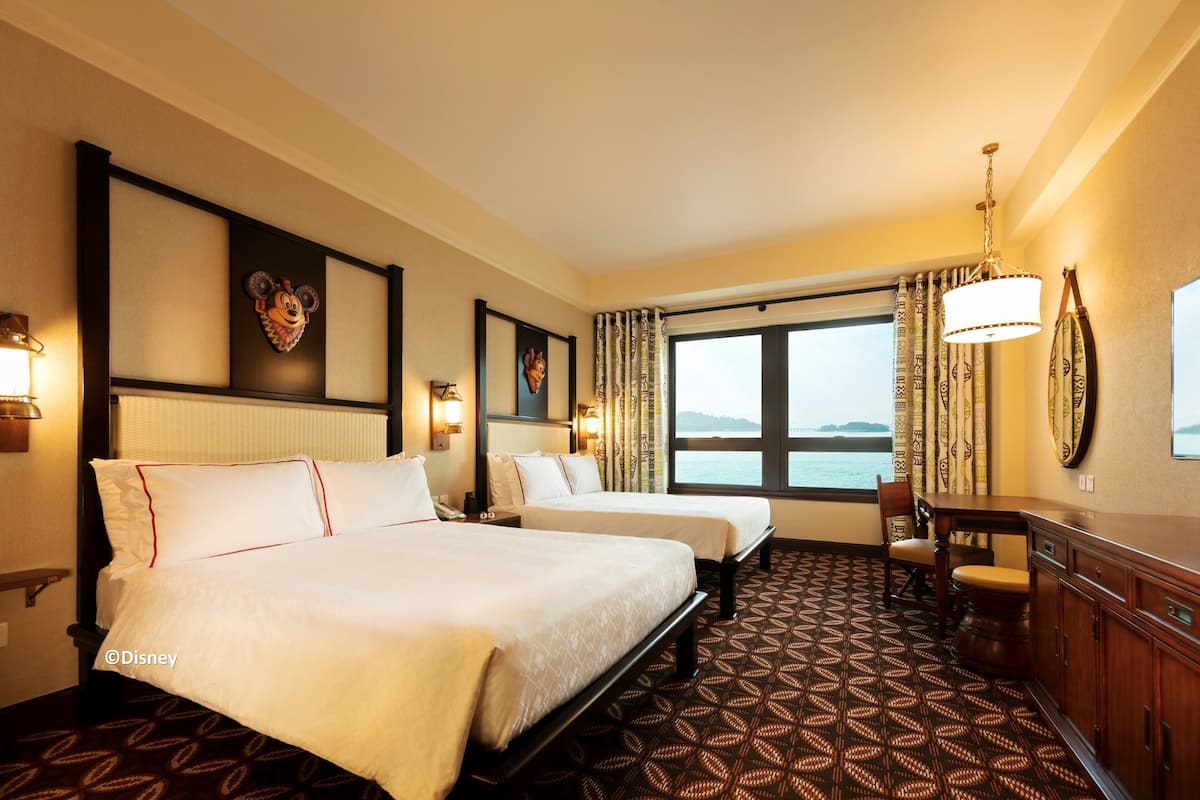A hotel room with two beds, a desk, and a view of the sea.