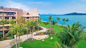 Un resort con vista a la playa, palmeras y un jardín bien cuidado.
