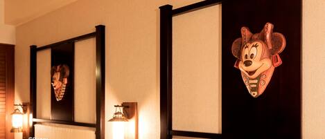 A hotel room with a Mickey Mouse head decoration on the wall, a mirror, and two wall-mounted lamps.