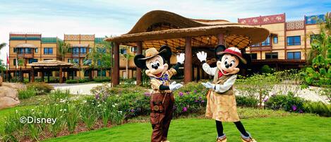 Mickey and Minnie Mouse in front of a building with a thatched roof and a garden.