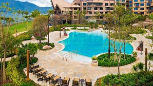 Un resort con piscina central, mobiliario exterior y montañas al fondo.