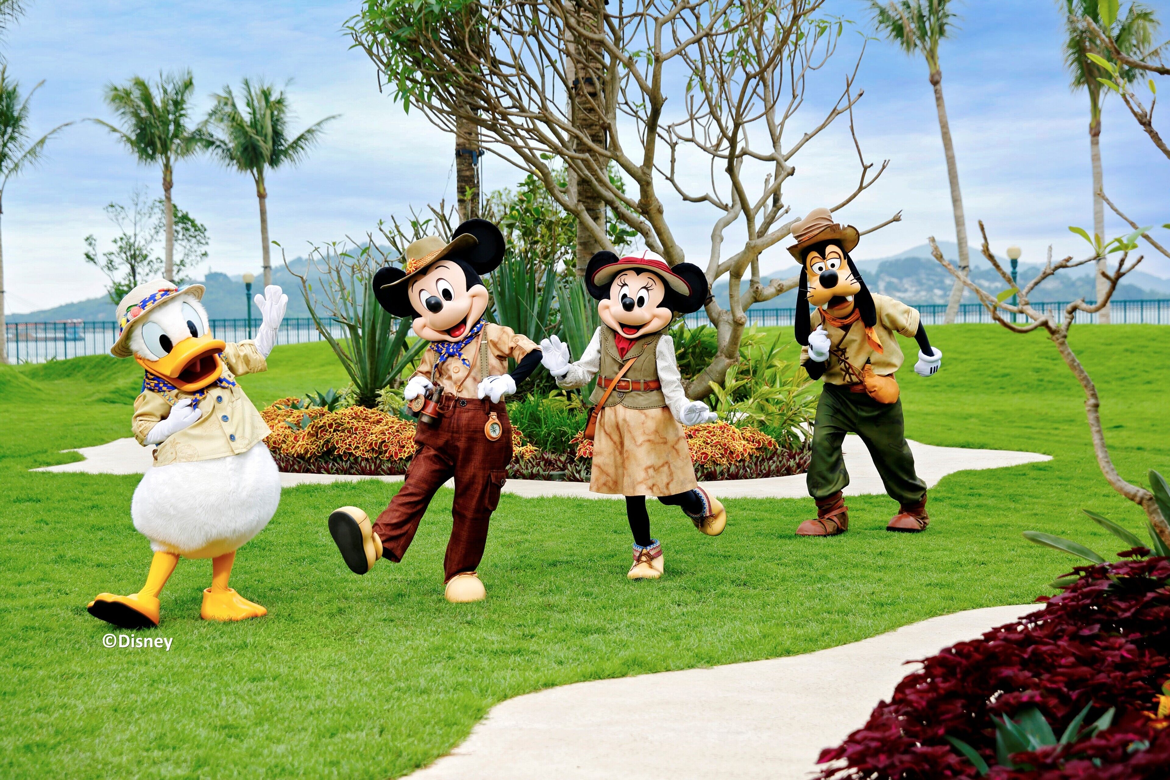 Three Disney characters in a grassy area with palm trees and a pathway.