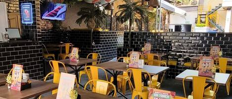 A restaurant with yellow chairs and tables, a blue ceiling, and various flags.