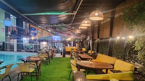 An indoor pool area with artificial grass, yellow and black seating, and hanging lights. - Maraca Hostel (Rio de Janeiro)