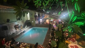 An indoor pool area with tables and chairs around the pool, surrounded by artificial foliage. - Maraca Hostel (Rio de Janeiro)