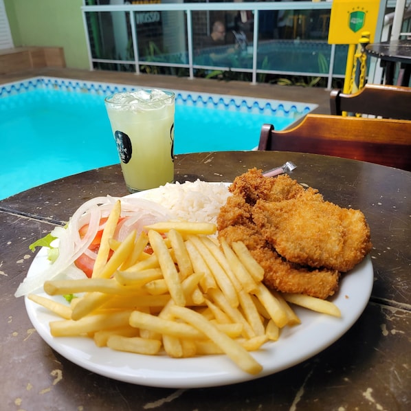A plate of food with fries, a salad, and a drink on a table near a pool.