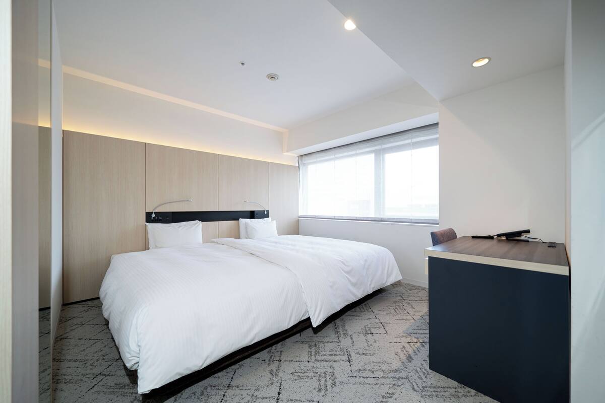 A modern hotel room with a bed, a desk, and a window.