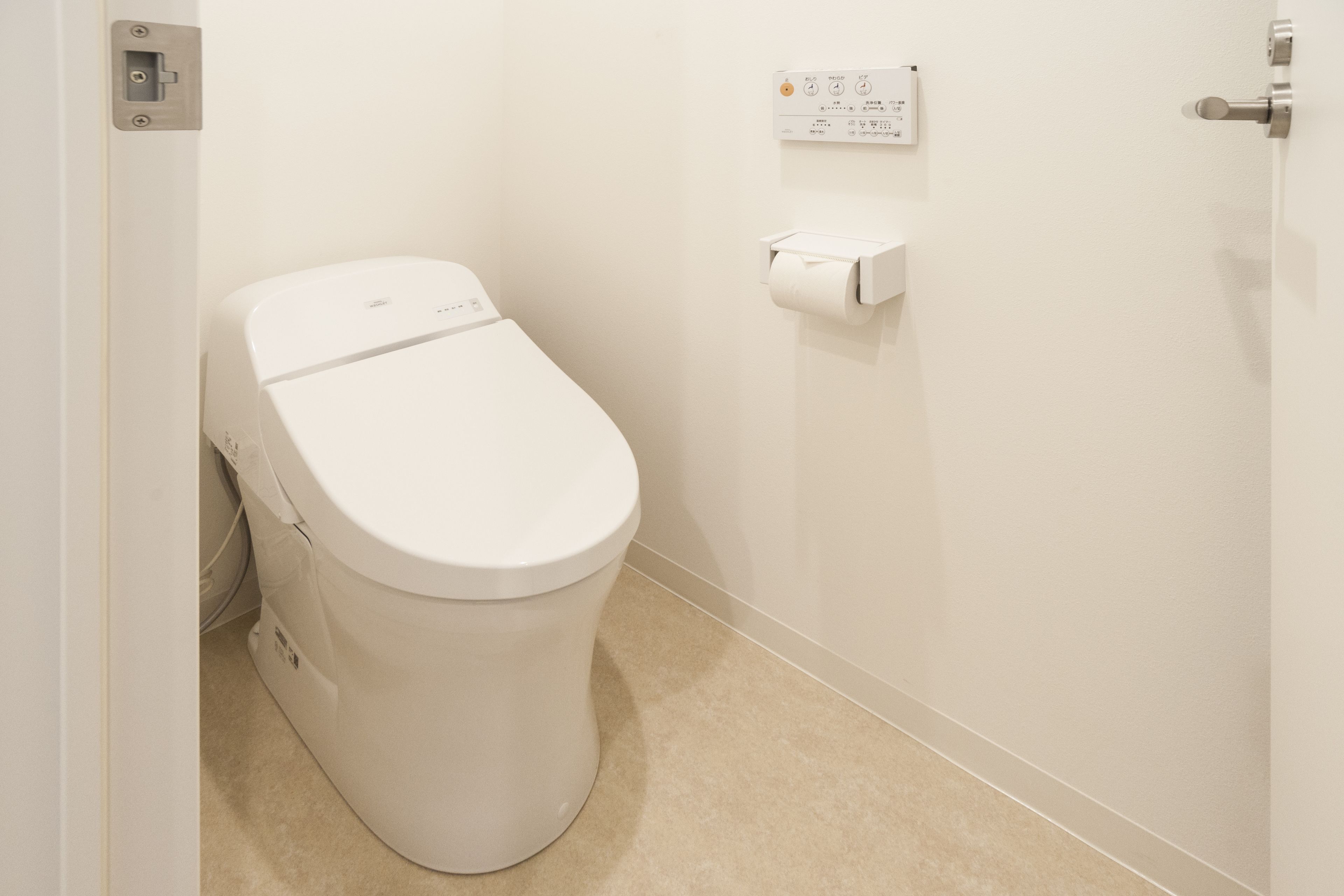 A white toilet with a flush handle, a toilet paper holder on the wall, and a beige floor.