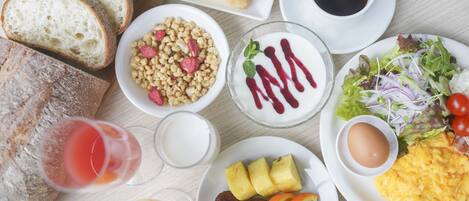 Una mesa de desayuno con cruasanes, pan, un tazón de cereal, un vaso de jugo, un plato de huevos, un tazón de yogur con bayas, una taza de café y una ensalada.