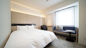A modern hotel room with a large bed, a desk, a seating area with a sofa and a small table, and a large window providing natural light. - Hotel Sunroute Tokushima (Tokushima)