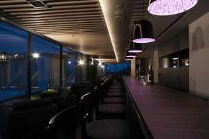 Uma área de bar moderna com um balcão comprido, várias cadeiras e iluminação pendente.