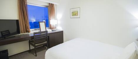 A hotel room with a bed, a desk with a chair, a television, and a window with curtains.