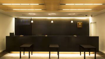 A reception area with a dark counter, three stools, and a wooden ceiling with recessed lighting.
