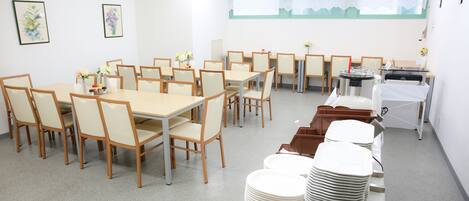 A conference room with multiple tables and chairs, a kitchenette, and a large window with a view.