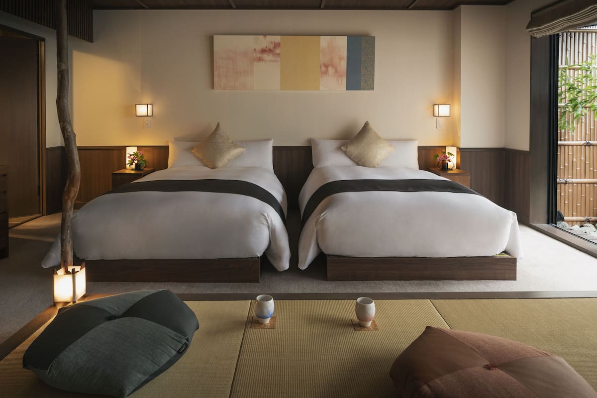 Ein modernes Hotelzimmer mit zwei Betten, einem großen abstrakten Gemälde, Nachttischlampen und Blick auf Bambus.