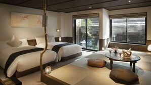 Een moderne hotelkamer met twee bedden, een tatami vloer, een klein tafeltje met een mand en uitzicht op het omliggende landschap door grote ramen.