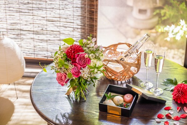 A table with a floral arrangement, champagne, glasses, and a box of chocolates.