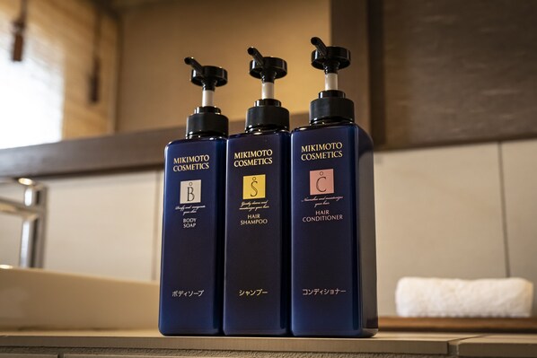 Tres botellas de productos de cosmética Mikimoto: jabón corporal, champú para cabello y acondicionador para cabello.