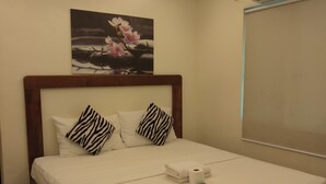 A neatly made bed with white linens, zebra-patterned pillows, and a single roll of toilet paper on the nightstand. - Giecel Pension (El Nido)